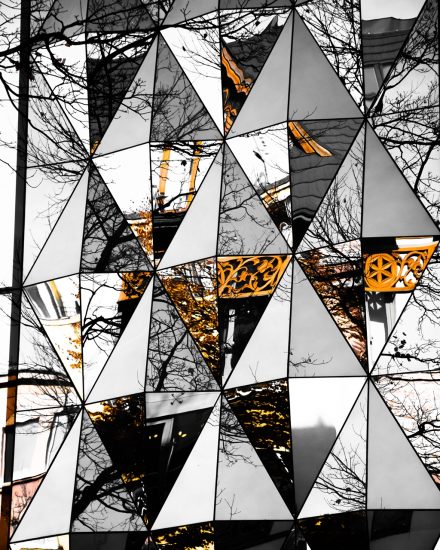 Zdjęcie. W trójkątach odbijają się drzewa i elementy architektury.