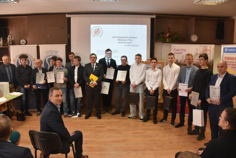 Grupa nagrodzonych uczestników konkursu ( z opiekunami) stoi w sali konferencyjnej. Na ekranie za ich plecami wyświetlona prezentacja z logo konkursu.