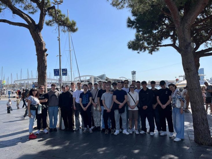 Grupa uczniów stoi pomiędzy dwoma drzewami.